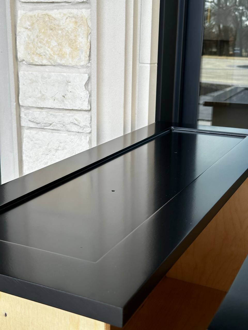 Black panel by a window, finished smooth enough to reflect the light